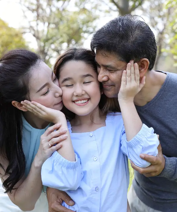 image of happy family, daughter putting her hands on parents cheek with smiling while father and mother kissing during summer time in the park